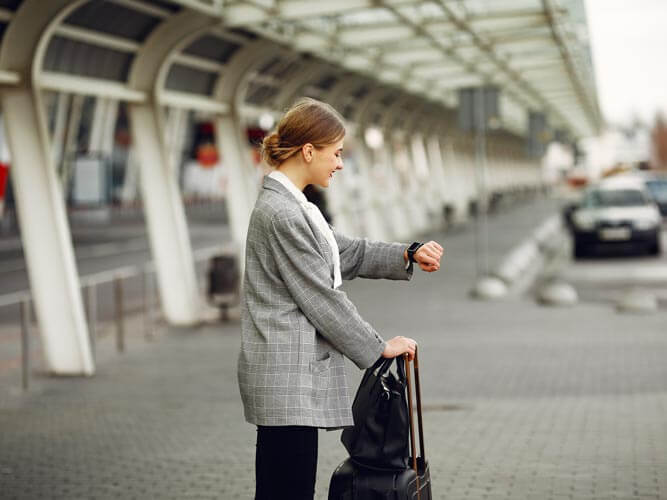 Business travel 2026: woman outside the airport looks at the time on her wristwatch