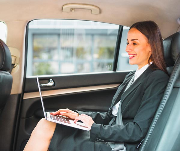 Chauffeur Service Milan: smiling businesswoman sitting inside car using laptop